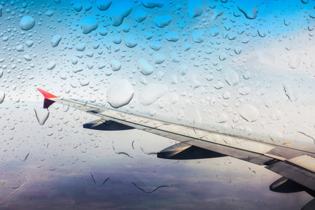 Raindrops on an airplane window during flight over a clear sky