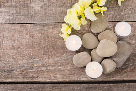 Decorative arrangement of pebbles, candles, and flowers on a rustic wooden surfaceの写真素材