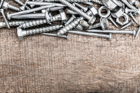 Various metal fasteners scattered on a wooden surface during afternoon lightの写真素材
