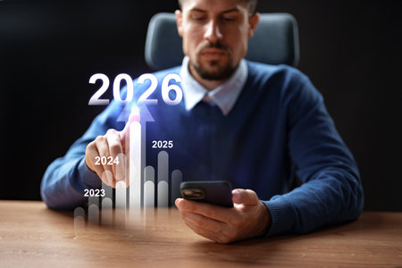 Man analyzing growth trends on smartphone while seated at desk in 2023の写真素材