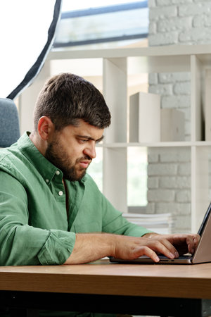Man working intently at a laptop in a modern office with bright lighting during the day