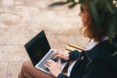 Young person working on a laptop while sitting on a bench in an outdoor spaceの写真素材