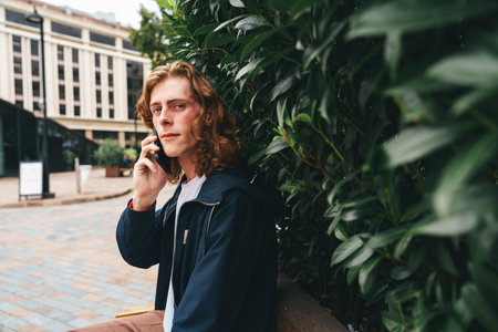 Young man talking on the phone in an urban setting surrounded by greenery