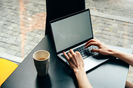 Individual working on a laptop at a cafe table during the day in an urban areaの写真素材