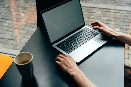 Person working on a laptop at a cafe table with a coffee cup nearby in the afternoonの写真素材