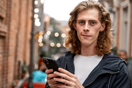 Young man using smartphone in a lively street with warm lights at dusk