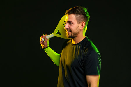 Man holds paddle and smiles in studio with dark background during sport practice session