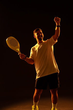 Man celebrating victory with a paddle racket in a dramatic lighting setupの写真素材