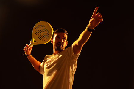 Skilled player demonstrating a powerful paddle tennis serve in dramatic lighting