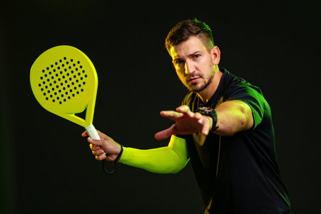 Man in black shirt prepares to hit a ball with a bright yellow paddle in a dark settingの写真素材