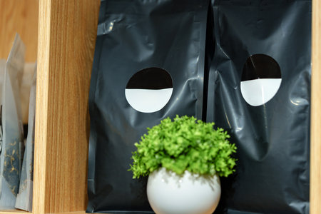 Coffee beans stored in black bags on a wooden shelf with a small green plant