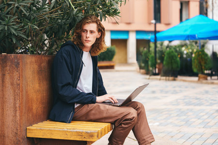 Young man works on laptop in outdoor setting during daytime in urban areaの写真素材