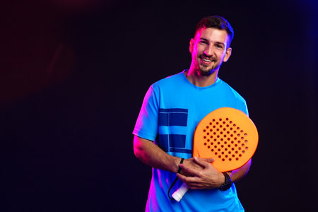 Man smiling while holding a bright orange paddle in a colorful studio settingの写真素材