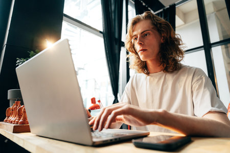 Young man working on a laptop in a modern cafe setting during the dayの写真素材