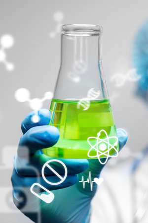 Scientist holds green liquid in laboratory flask during chemical experimentの写真素材