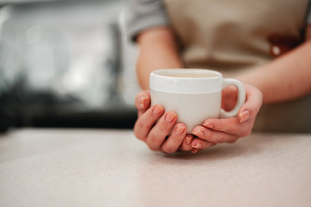 Warm cup held by barista at cozy cafe counter during morning rushの写真素材