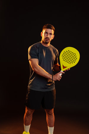 Man holding a bright yellow paddle for an indoor racket sport in a dark settingの写真素材