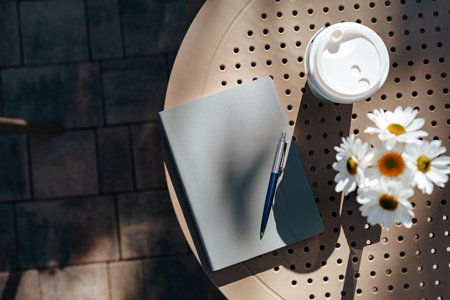 Notebook, pen, coffee, and flowers on a sunny outdoor table