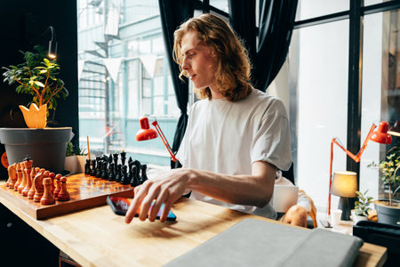 Young man enjoying a chess game in a cozy indoor space with plants