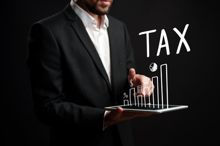 Businessman presenting tax data on tablet with graphs and symbols during a dark backgroundの写真素材