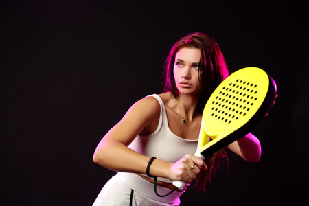 Young woman practicing paddle tennis indoors with focused expression in dramatic lightingの写真素材