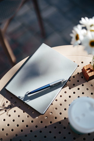 Notepad and pen on a table in an outdoor cafe with sunny ambianceの写真素材