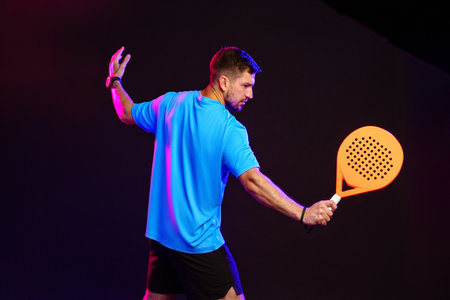 Man plays paddle sports with bright orange racket in studio lightingの写真素材