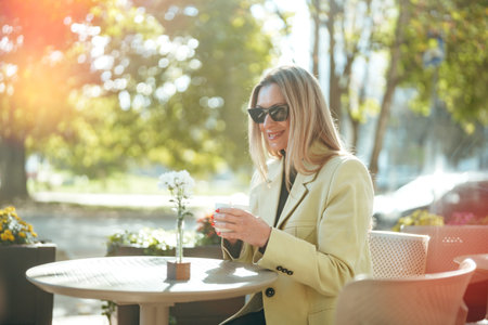 Woman enjoying coffee outdoors on a sunny day in a lively urban settingの写真素材