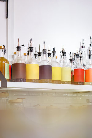 Colorful bottles with various liquids displayed on a shelf in a bright cafe settingの写真素材