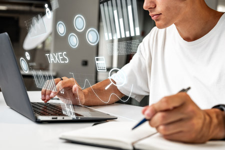 Young adult working on financial data analysis at a desk with a laptop and notebookの写真素材