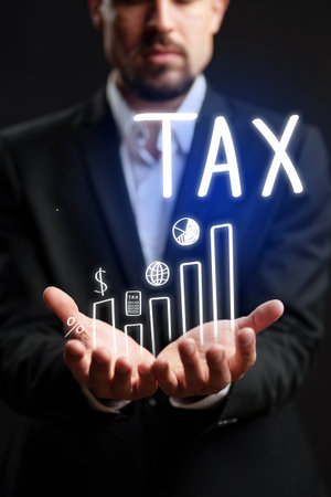 Businessman holding graphs related to tax trends and financial growth in dark settingの写真素材