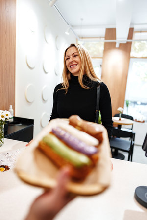 Smiling woman enjoying colorful pastries at a cozy cafe in autumnの写真素材