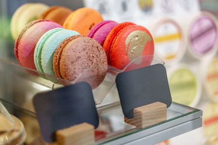 Colorful macarons displayed in a dessert shop case during a sunny afternoonの写真素材