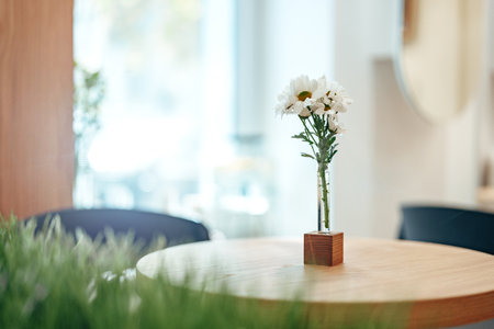 Bright flowers in a vase on a wooden table in a cozy cafe setting during the afternoonの写真素材