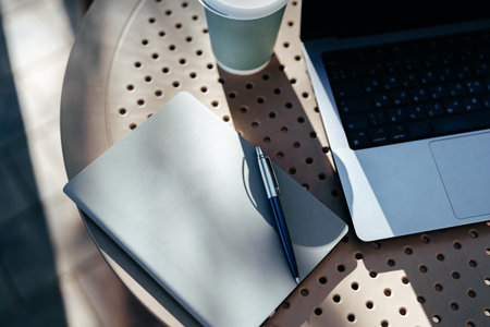 Notebook and laptop on outdoor table with coffee in sunny environmentの写真素材