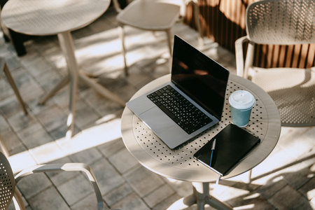Working at an outdoor cafe with a laptop and a cup of coffee on a sunny dayの写真素材