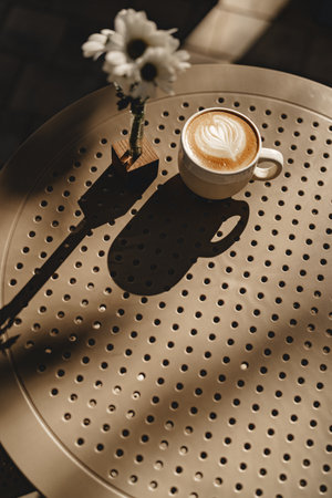 Coffee cup on a sunlit table with flowers in a cozy cafe settingの写真素材