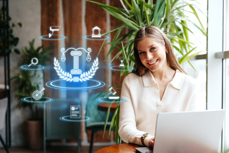 Young woman using laptop with legal icons in modern workspace surrounded by plantsの写真素材