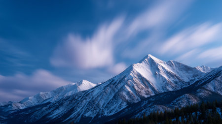 Majestic snow-covered mountains stand against a clear blue sky at sunsetの素材