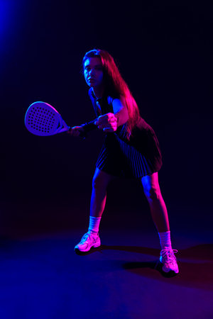 Young athlete practices racquet sports against a dark background with colorful lightingの写真素材