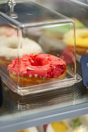 Bright pink donut covered in sprinkles displayed in pastry showcase at bakeryの写真素材