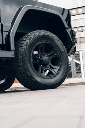 Black SUV with stylish wheel parked on the street near modern buildings