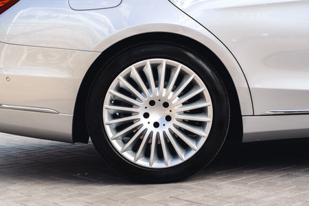 Luxury silver car with detailed alloy wheel parked on smooth pavement in sunlight