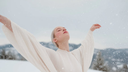 Woman enjoying snowfall in the mountains, arms open wide, winter scene capturedの素材