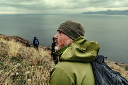 Hikers exploring a rugged coastline under a cloudy sky near the ocean in a remote location
