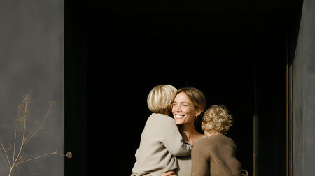Mother hugs children in warm embrace at home entrance during morning lightの素材