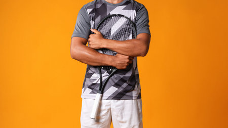 Tennis player stands with racket and smiles in studio against orange backgroundの写真素材