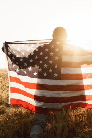 Person stands in field holding large American flag during sunsetの写真素材