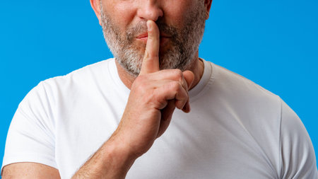 Man showing a quiet gesture with finger on lips against a blue background