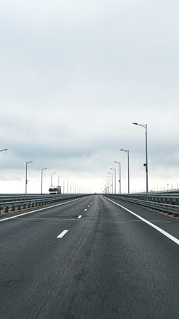 Road extends into distance with cloudy sky above and light posts lining sidesの写真素材